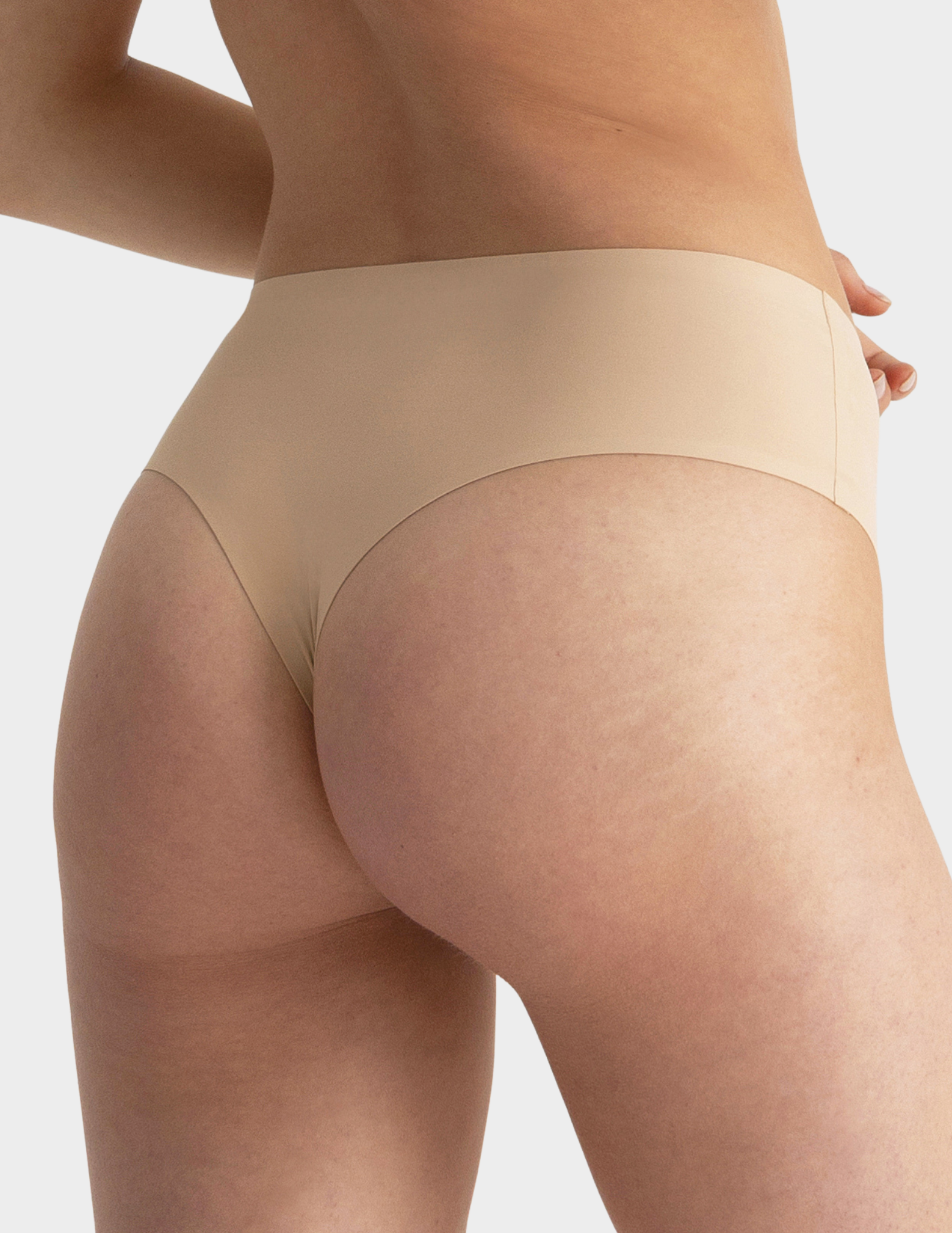 Back view of a model wearing Evelyn & Bobbie Seamless Thong in Sand