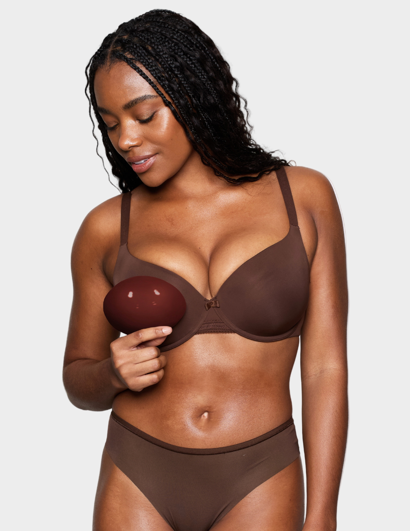 Woman wearing a brown bra and underwear set holding a brown bra insert.