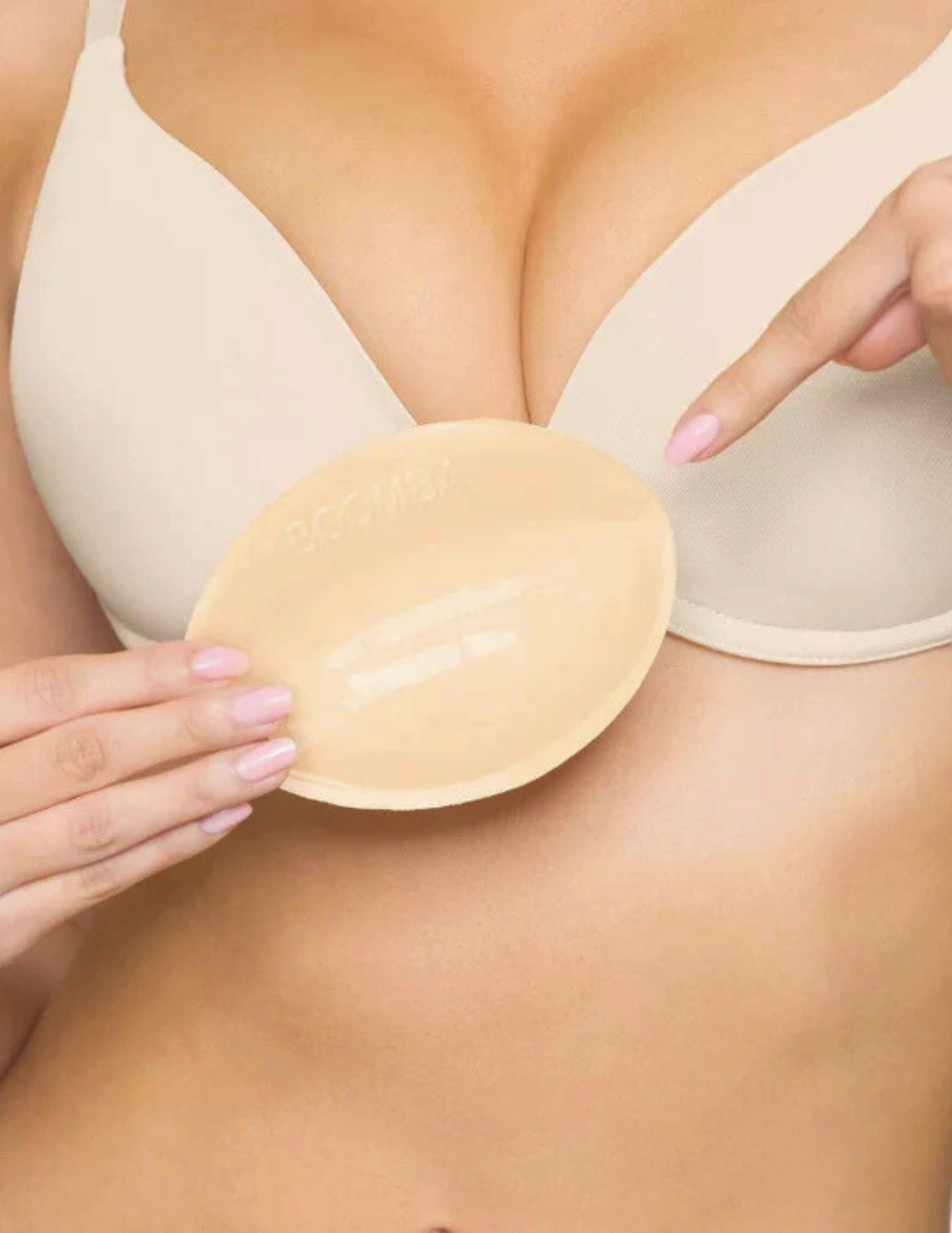 Closeup of woman holding and pointing to beige Boomba bra insert