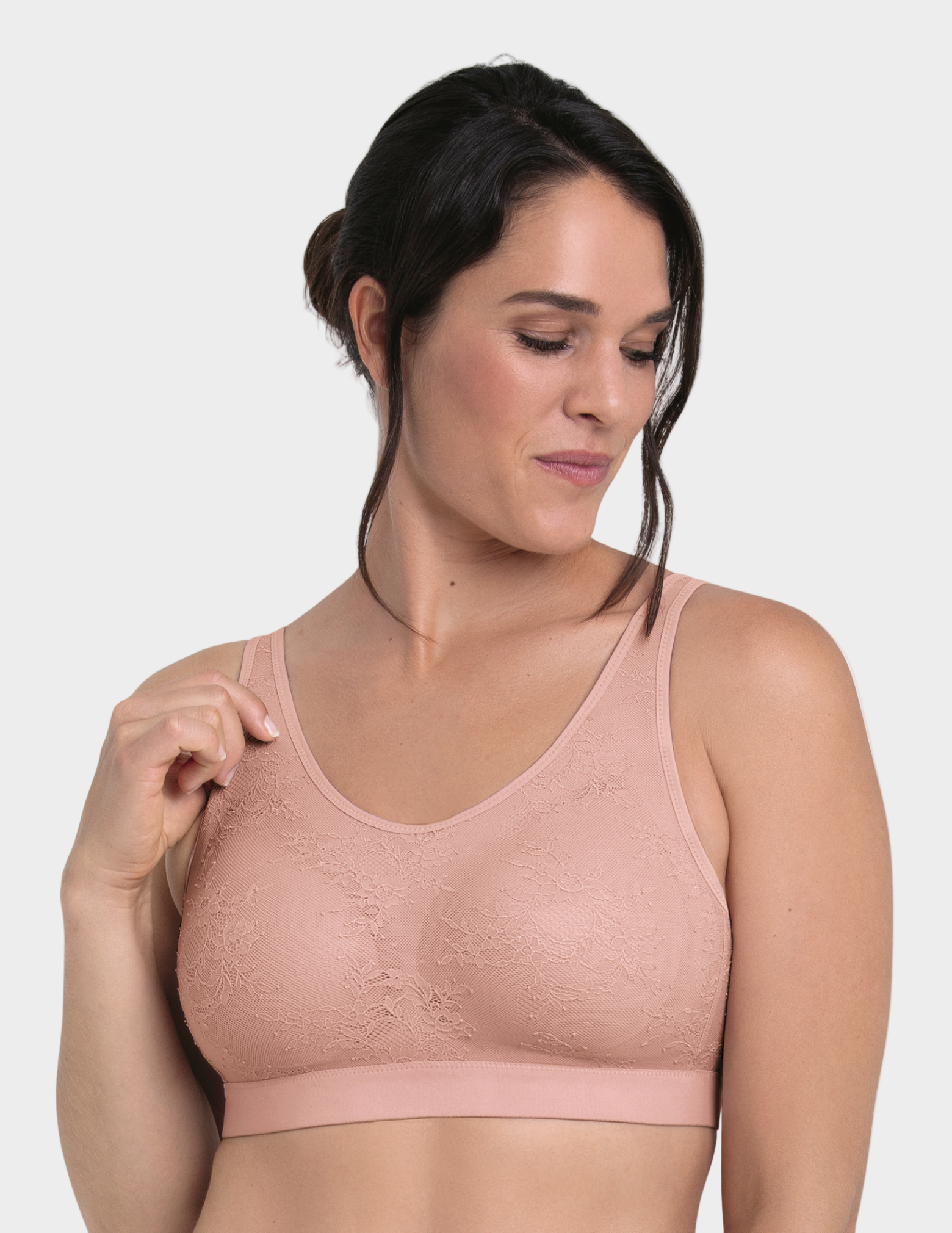 Woman wearing a light pink bralette against a plain background
