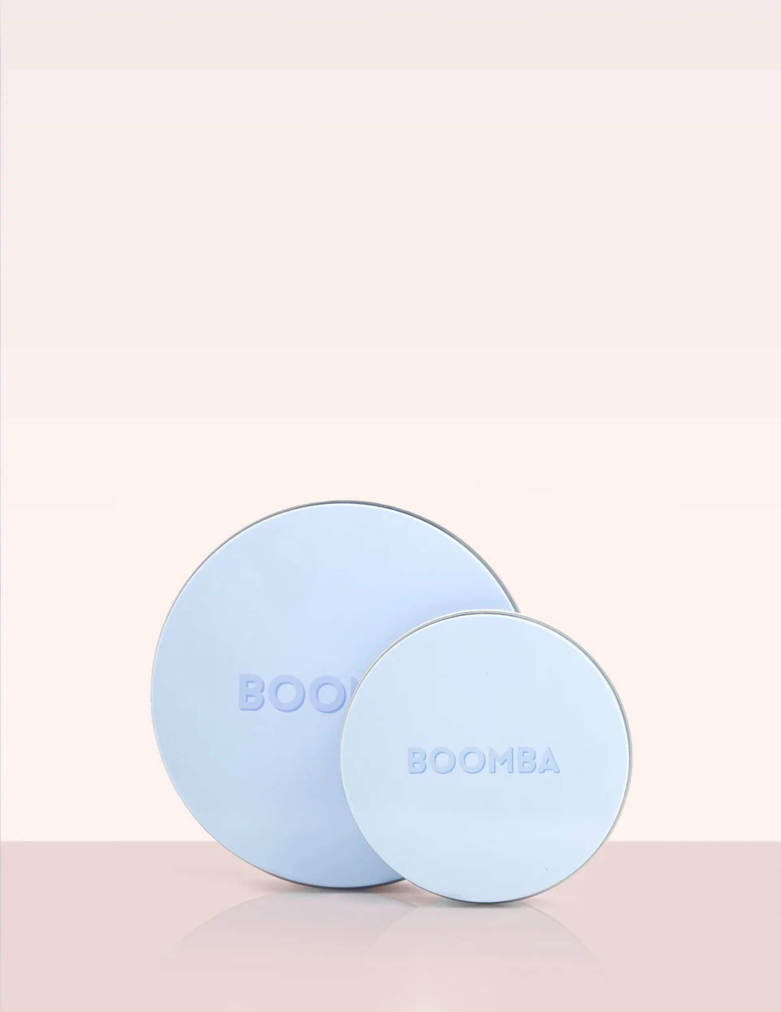 two different sized round blue containers labeled "BOOMBA" on a pink backdrop