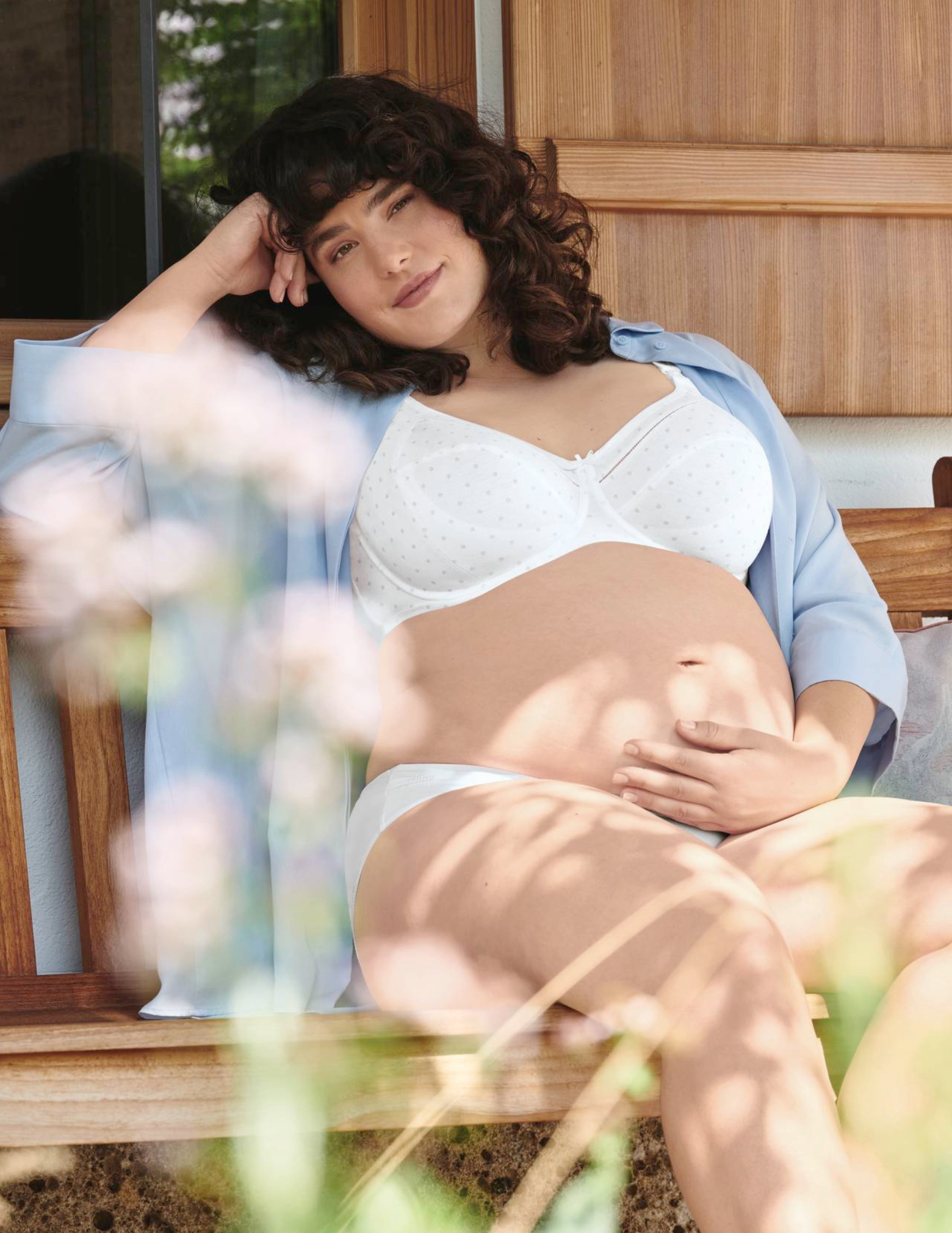 Pregnant woman sitting on a wooden bench wearing a white nursing bra.