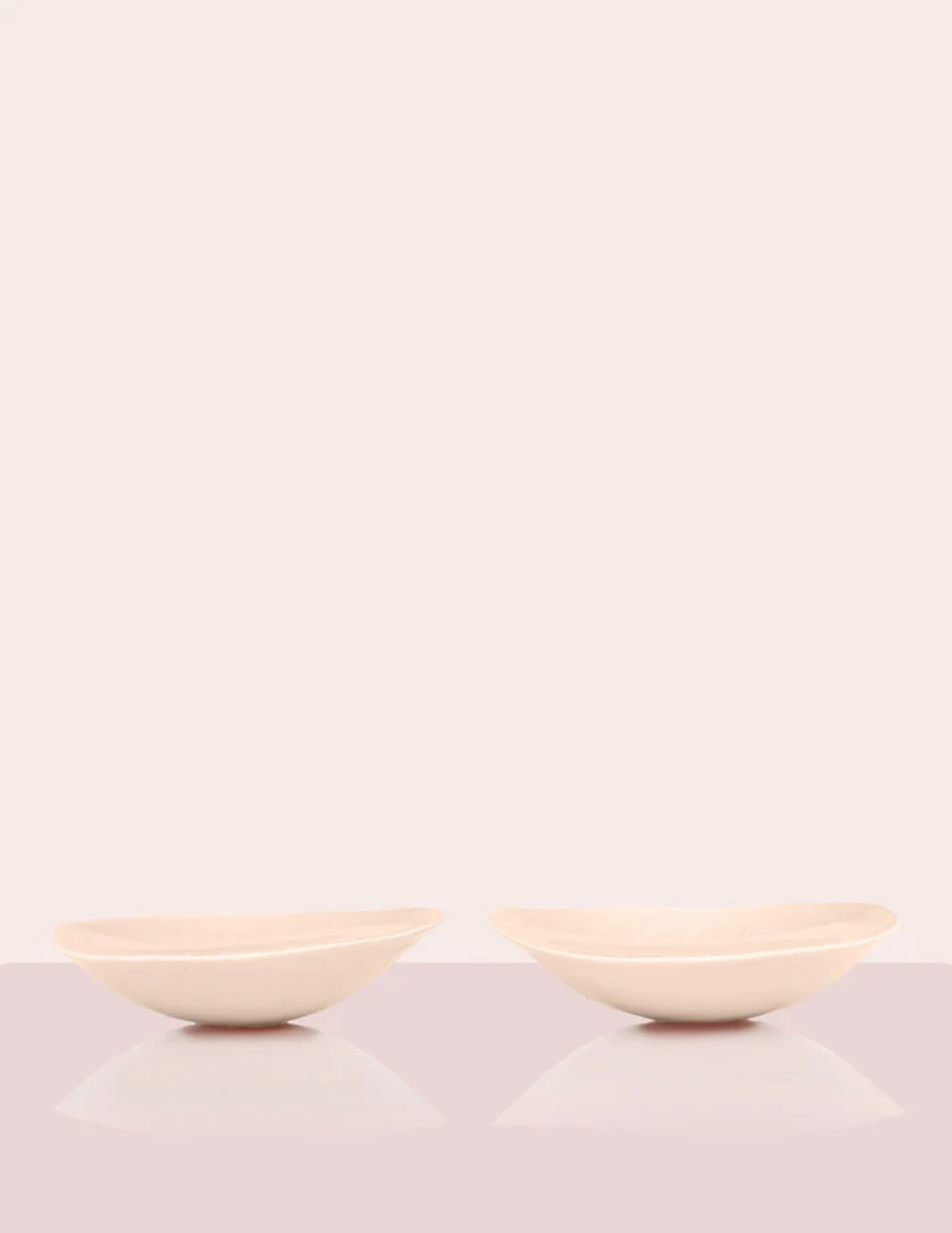 side view of two beige padded bra inserts laying on table