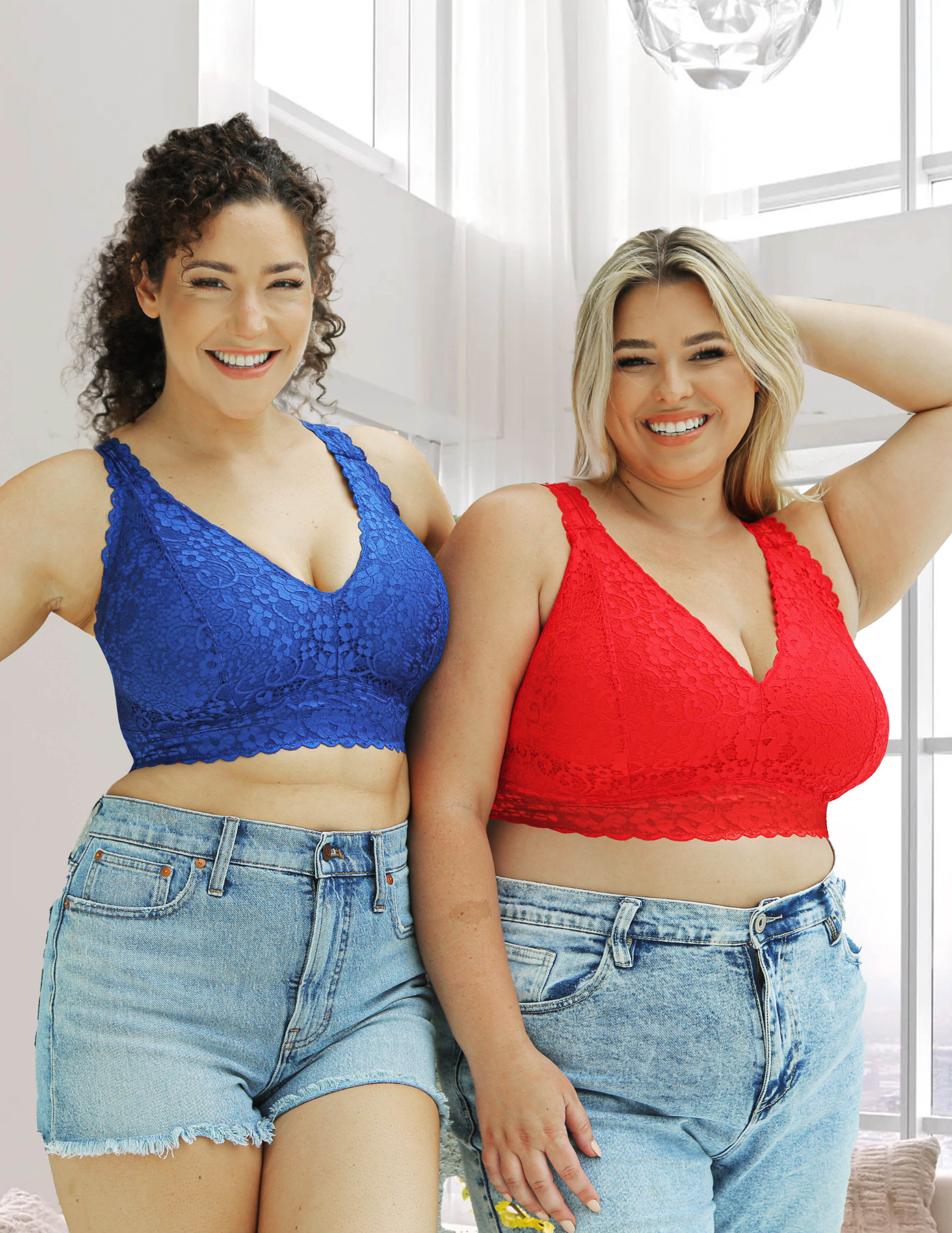 Two women wearing blue and red lace bralettes with jeans indoors.