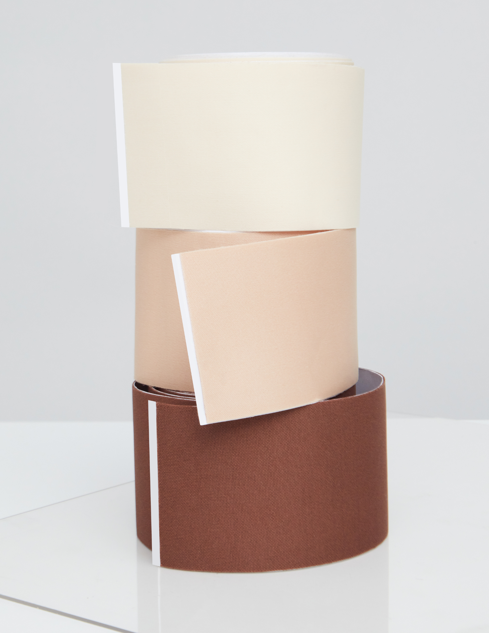 3 stacked rolls of body tape in beige and brown on a white background