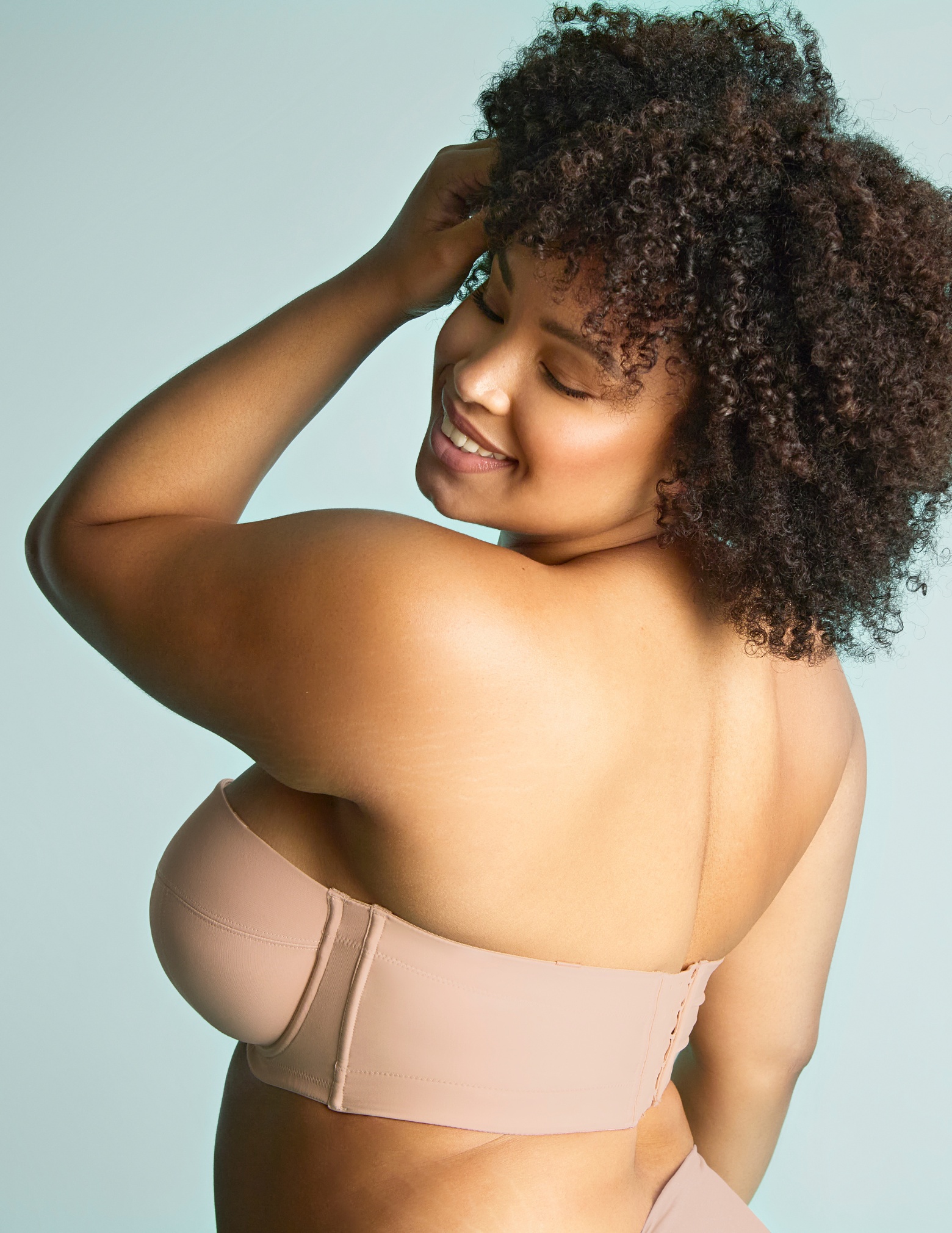 Woman smiling wearing dana strapless bra in linen against a blue background