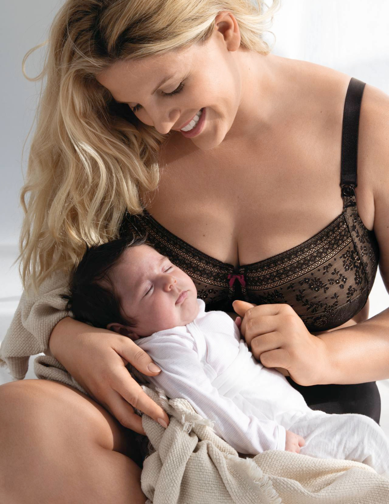 Woman in a black lace nursing bra holding a baby wrapped in a blanket.