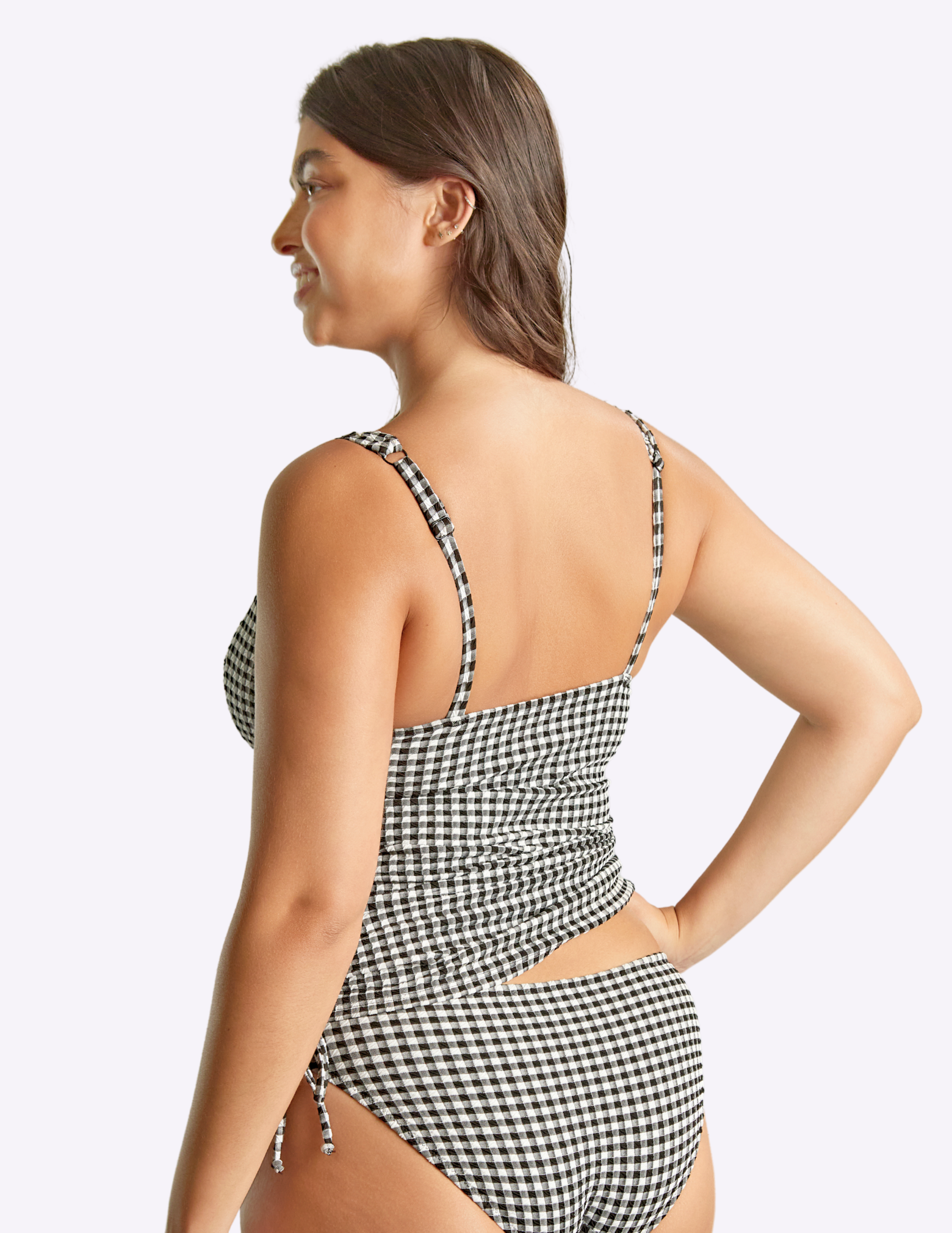 Woman facing away from camera wearing a black and white checkered swimsuit on a light gray background