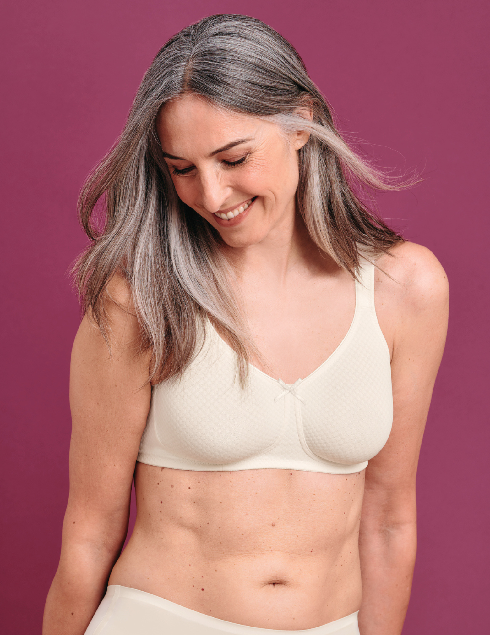 Woman wearing an off white bra against a magenta background