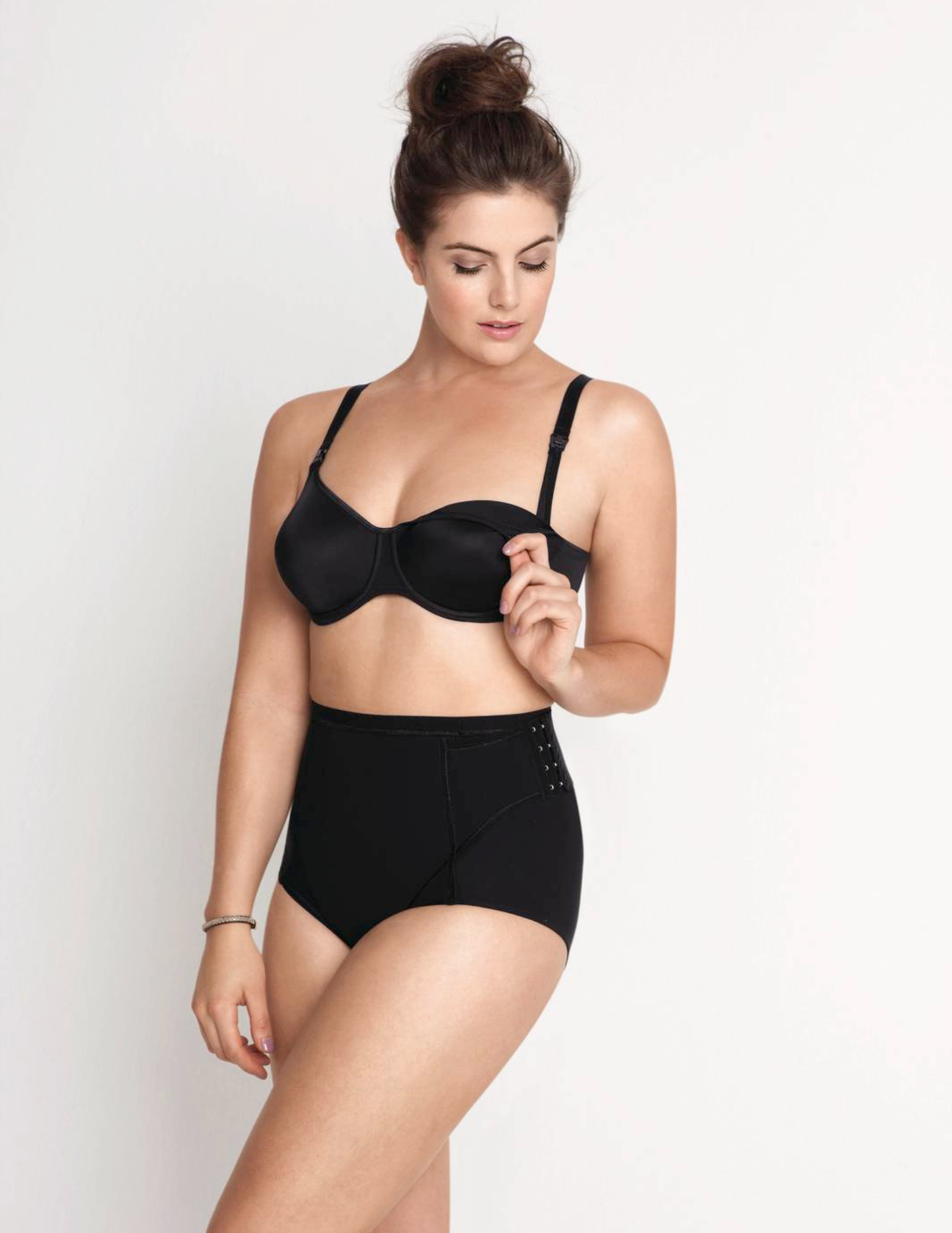 Woman wearing a black nursing bra unclipped and high-waisted underwear on a white background