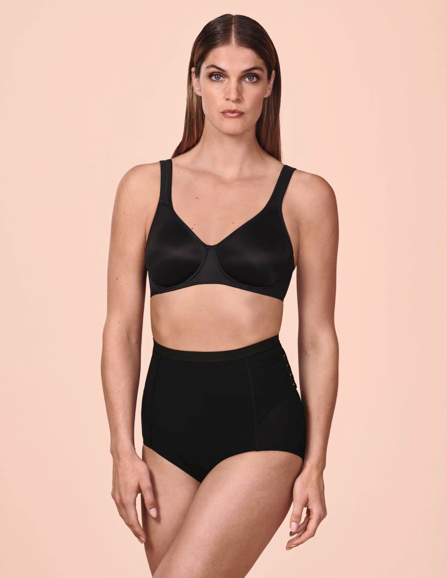 Woman wearing a black bra and panty set on a pink background